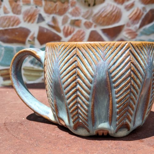Carved Mug with Blue Glaze in front of a mosaic wall