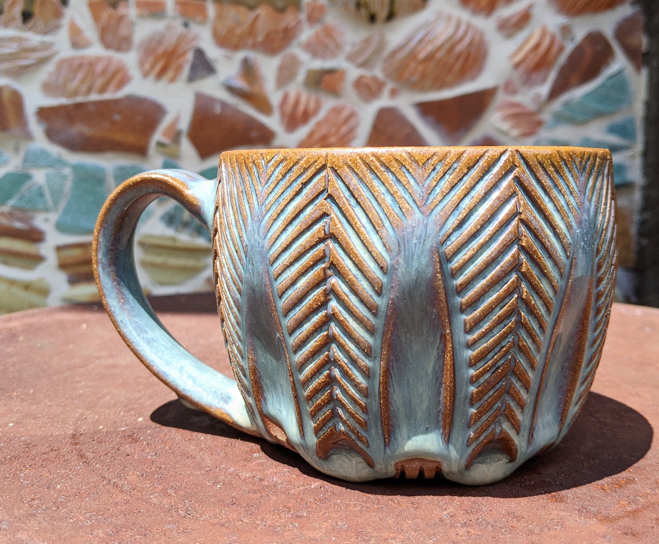 Carved Mug with Blue Glaze in front of a mosaic wall